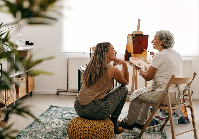 A woman painting whilst engaged in conversation in with another woman.