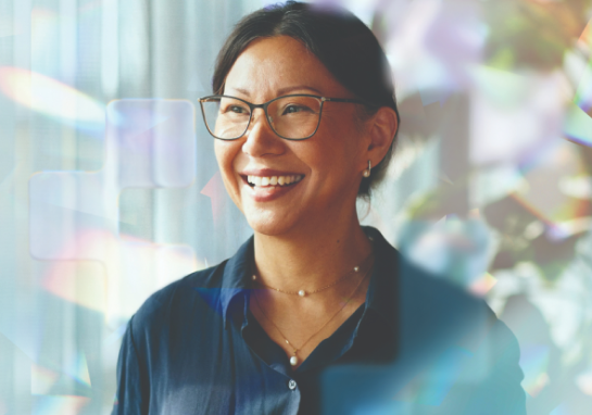 Person wearing glasses in an office setting, standing near a window with soft light and abstract reflections in the foreground.