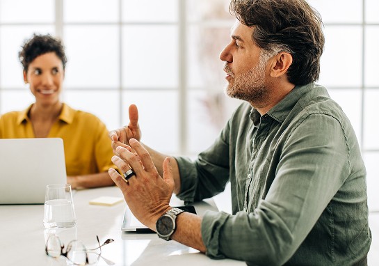 A man and woman collaborate at a table with a laptop, appearing engaged in conversation.