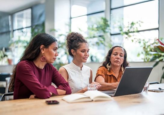 Three First Nations women use a laptop in a classroom