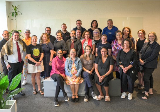A team of individuals posing happily for a photo in a well-lit office space.