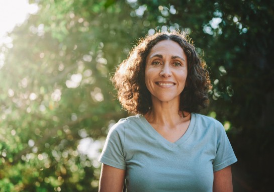 A woman smiling with a sunlit tree behind her