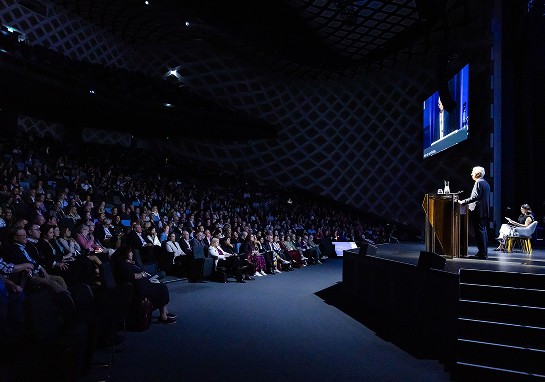 A man delivering a speech at a conference, addressing an engaged audience seated in front of him.