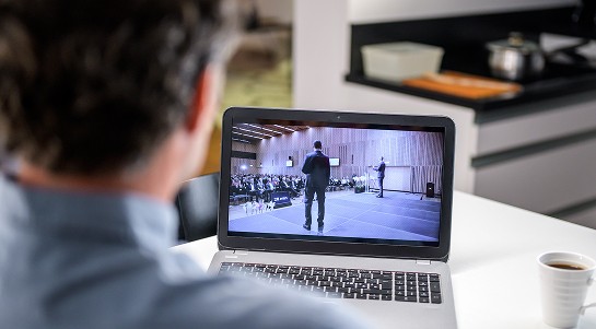 A man sits at a desk, intently watching a video on his laptop screen.