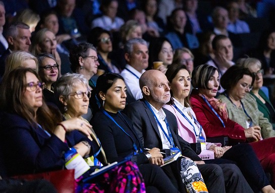Several individuals sitting in a row, engaged in an event, showcasing a variety of expressions and attire.