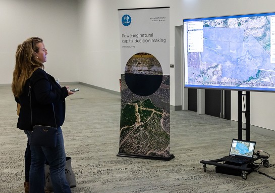 Two individuals standing in front of a large screen, engaged in discussion or presentation.