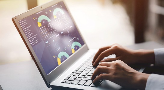 A person types on a laptop displaying various graphs and data visualisations.