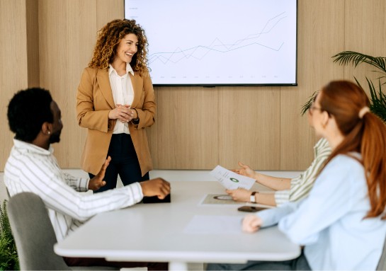A woman delivers a presentation to her colleagues, using slides to illustrate her points in a conference room.