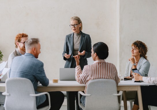 A woman in a business suit presents to her colleagues in a conference room, engaging them with her ideas.