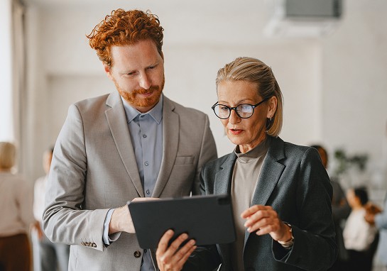 A man and woman in business attire are collaborating while looking at a tablet together.