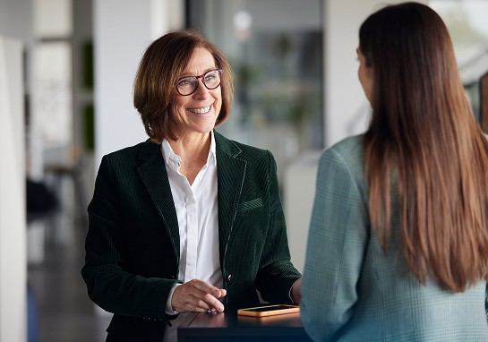 A woman in a business suit engages in conversation with another woman in a professional setting.