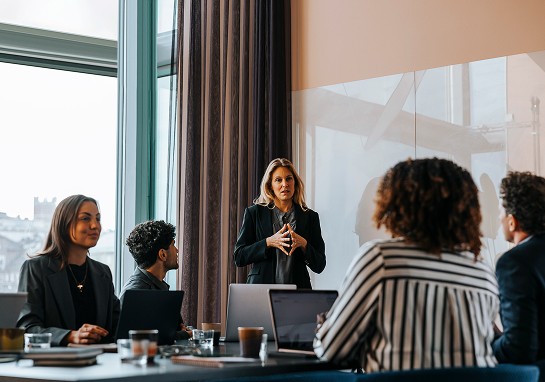 A woman stands before a group, delivering a presentation and interacting with her audience.