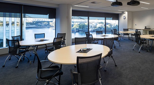 Interior of a conference room with tables and chairs set up near a window, allowing for ample daylight.