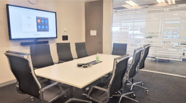 Conference room with a large screen, chairs, and a frosted glass wall, designed for 8 people in a boardroom format.