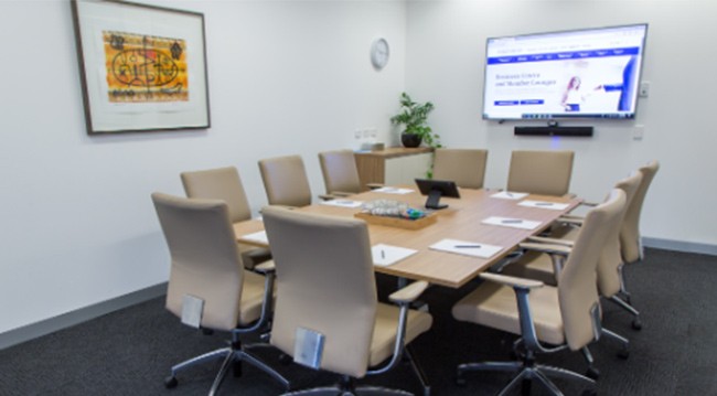 A boardroom setup with a large screen, chairs, whiteboard, and frosted glass wall, suitable for 8 attendees in the Barwon Room.