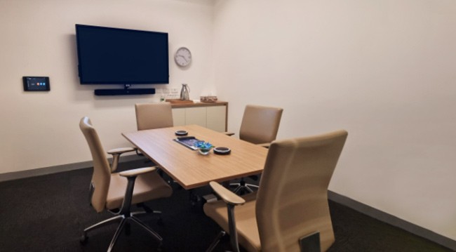 Small conference room with a TV, seating for four, whiteboard, and frosted glass wall, ideal for boardroom discussions.