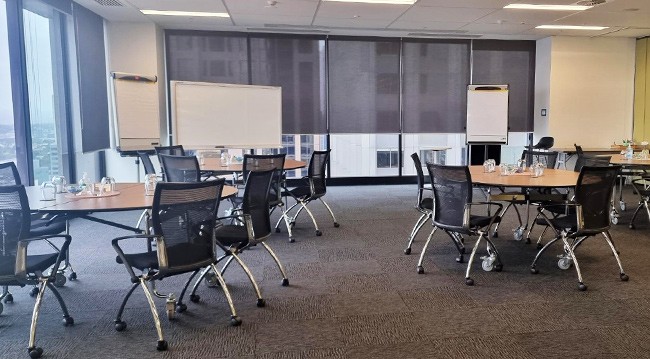  Spacious conference room with tables and chairs, large window showcasing Melbourne, equipped for presentations and meetings.