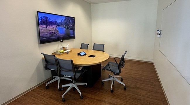 Modern conference room for 5, equipped with a large flat screen TV, whiteboard, and glass wall to the member lounge.