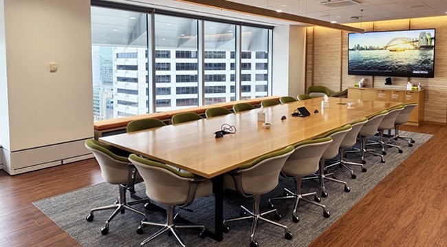 Conference room with large table and chairs, TV screen, whiteboard, and view of Sydney, accommodating 18 people.