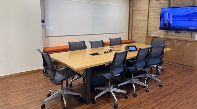 Conference room featuring a large table, chairs, TV screen, whiteboard, and frosted glass wall, accommodating 8 people.