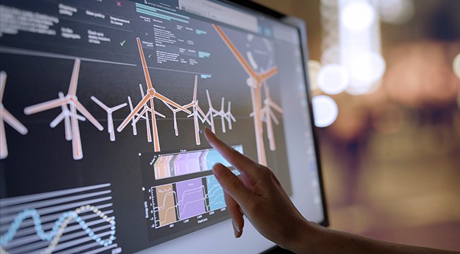Stock image showing a woman’s hand using a touch screen monitor. The monitor displays data, images & moving graphics.